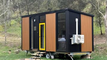 A small, modern mobile home with a sliding door, an air conditioning unit, and a portable table.