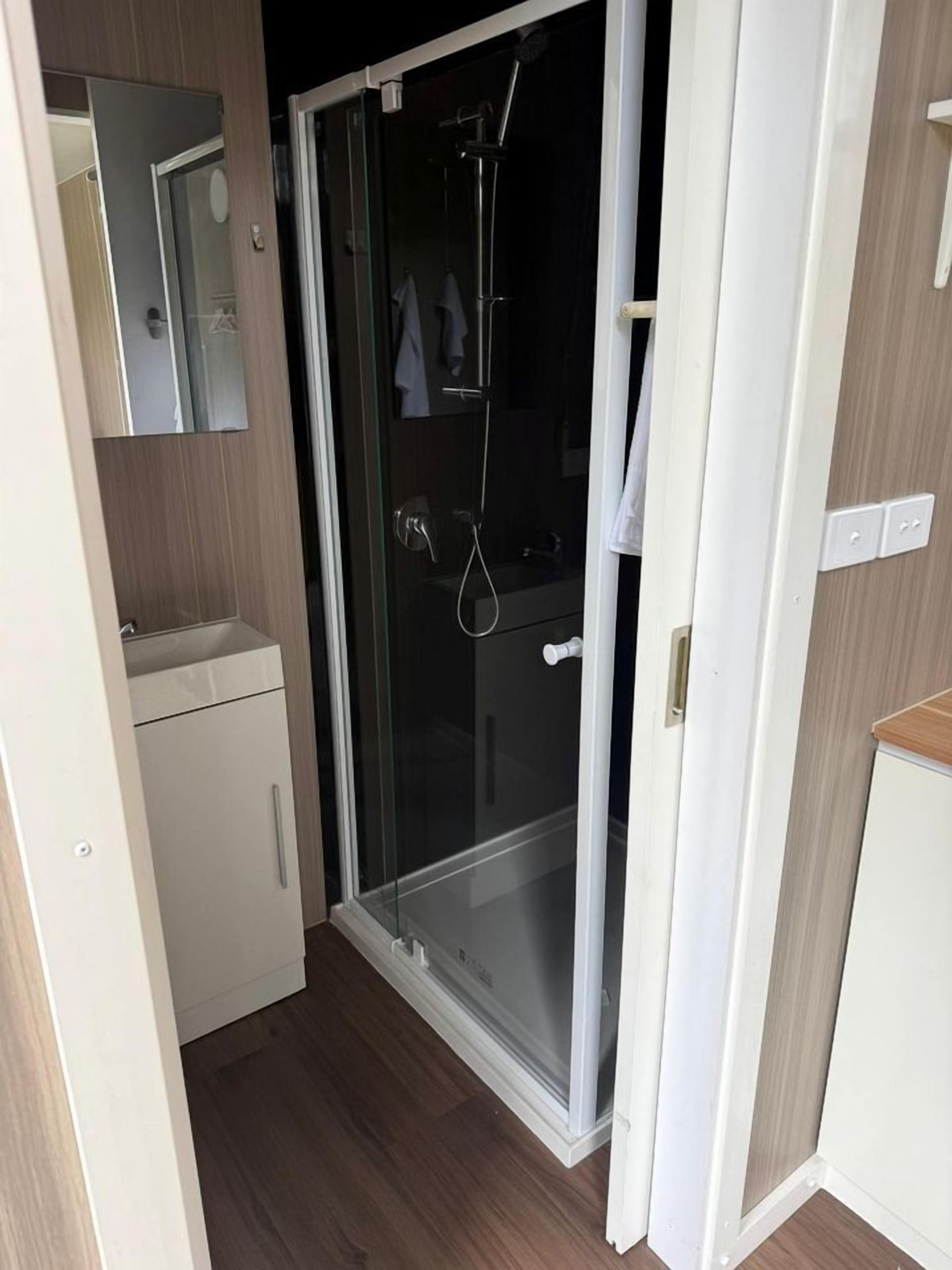 Un bany amb dutxa d'ampul·la de vidre, un lavabo blanc i un mirall.