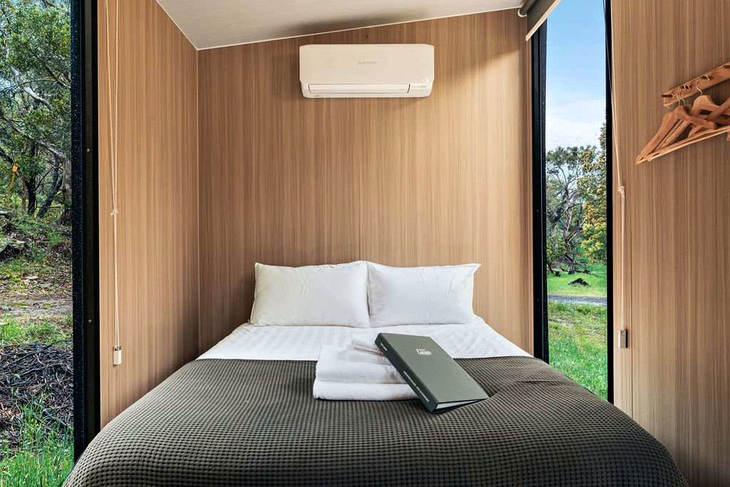 Ein Schlafzimmer mit einem Bett, weißen Kissen, einem Laptop und einer Klimaanlage.