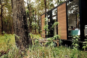 A cabin with a wooden exterior, large windows, and a visible interior with a bed and a table. - Cozy Tiny House with Bushland Views and Firepit in Mullaway, Australia (Mullaway)