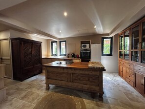 A spacious kitchen with a central island, wooden cabinetry, and a tiled floor. - Peaceful Haven on the Banks of the Dordogne — Pool and Charm (Saint-Antoine-de-Breuilh)