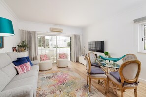 Ein modernes Wohnzimmer mit einer Couch, Sesseln, einem Glastisch und einem an der Wand montierten Fernseher.