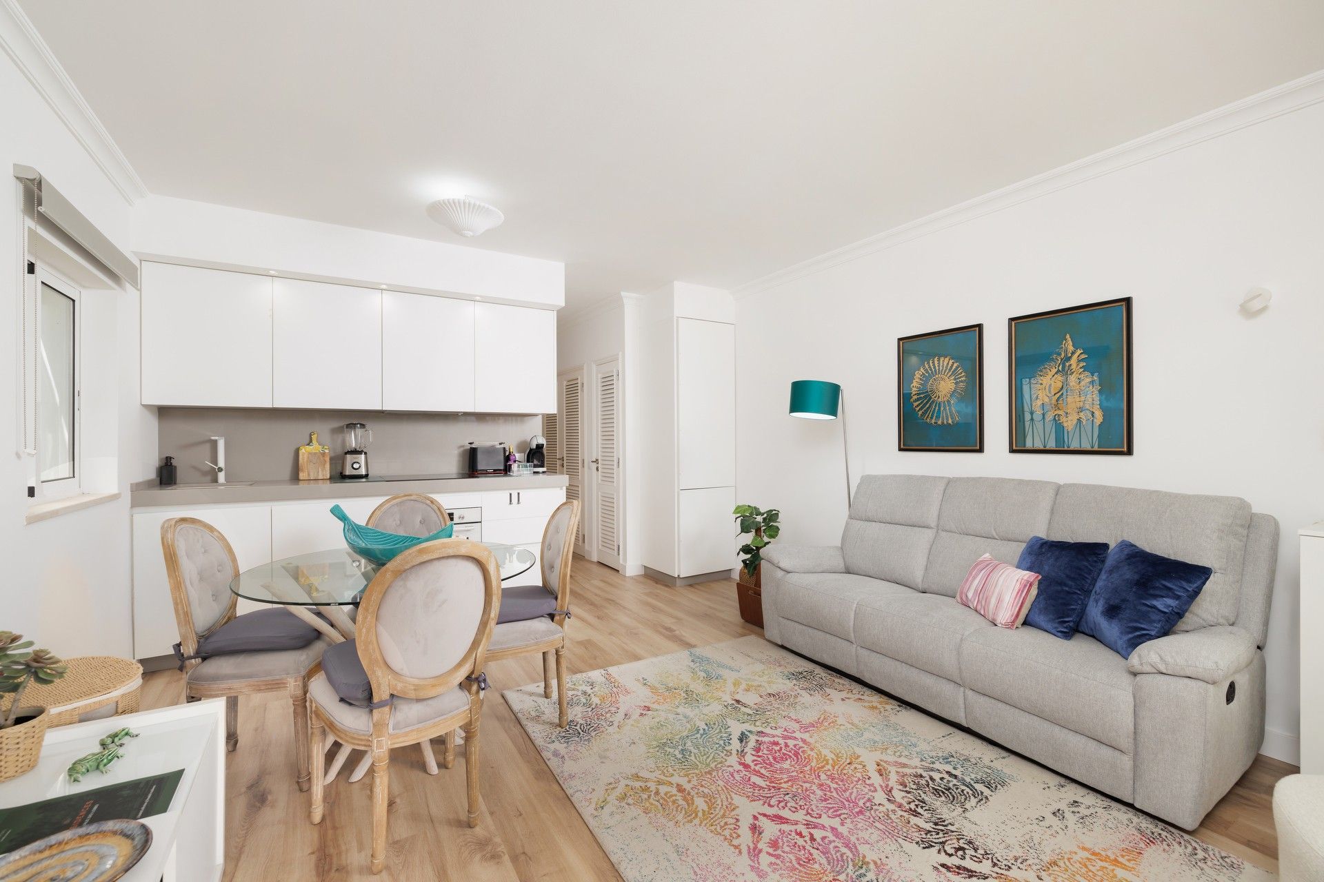 Ein modernes Wohnzimmer mit einem grauen Sofa, einem Glastisch und einem farbenfrohen Teppich.