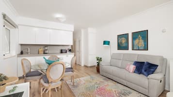 Ein modernes Wohnzimmer mit einem grauen Sofa, einem Glastisch und einem farbenfrohen Teppich.