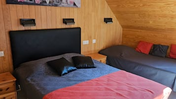 Ein Schlafzimmer mit schrägem Dach, einem Bett mit roter Decke, einem grauen Sofa und einem Gemälde an der Wand.