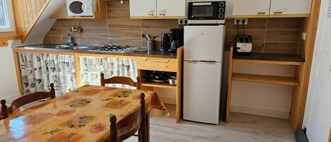 A compact kitchen with a gas stove, microwave, refrigerator, and a small dining area with a table and chairs.