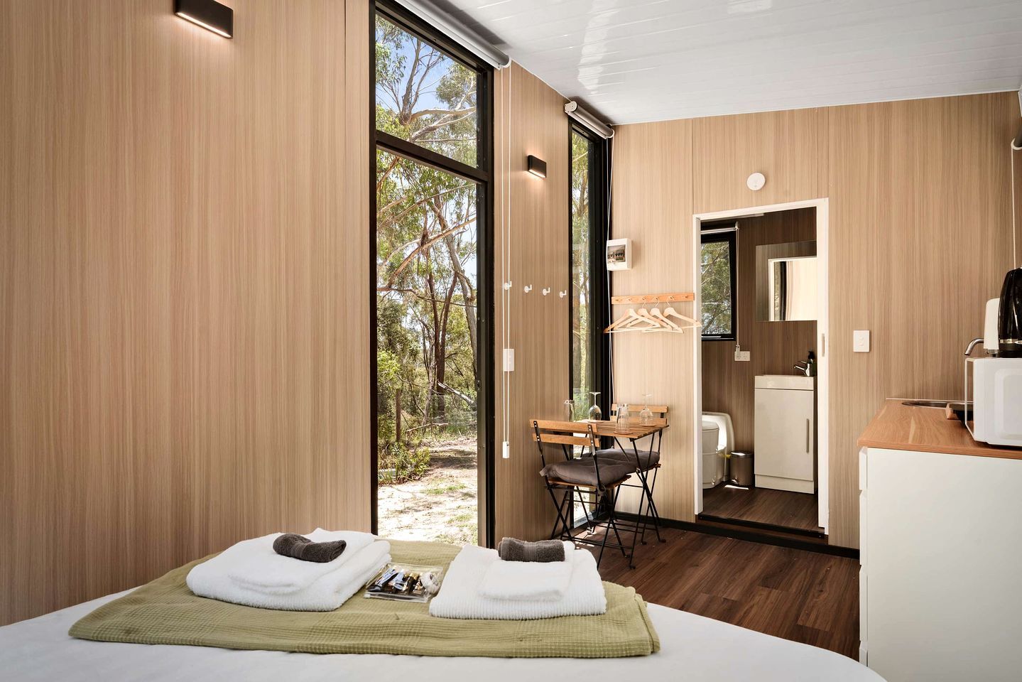 A modern hotel room with a large window, a small dining area, and a kitchenette.