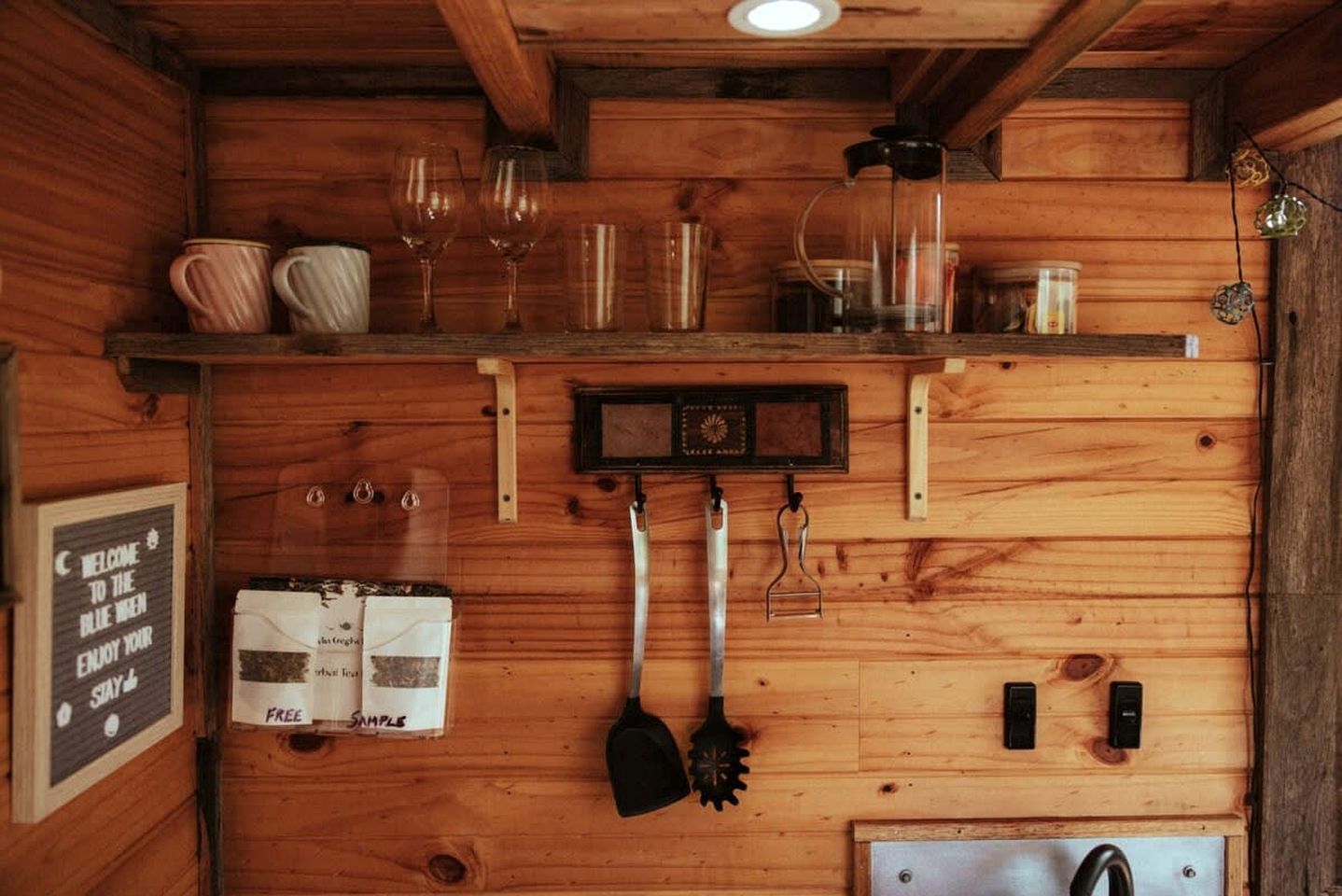 A wooden interior with a shelf holding glasses and jars, a clock, and a sign offering free samples.