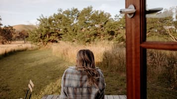 A person seated on a wooden deck with a view of a grassy field and trees.