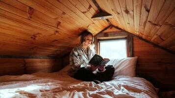 A person sitting on a bed in a wooden room with a sloped ceiling and a window.