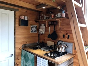 A compact kitchen with a sink, stove, and hanging utensils.