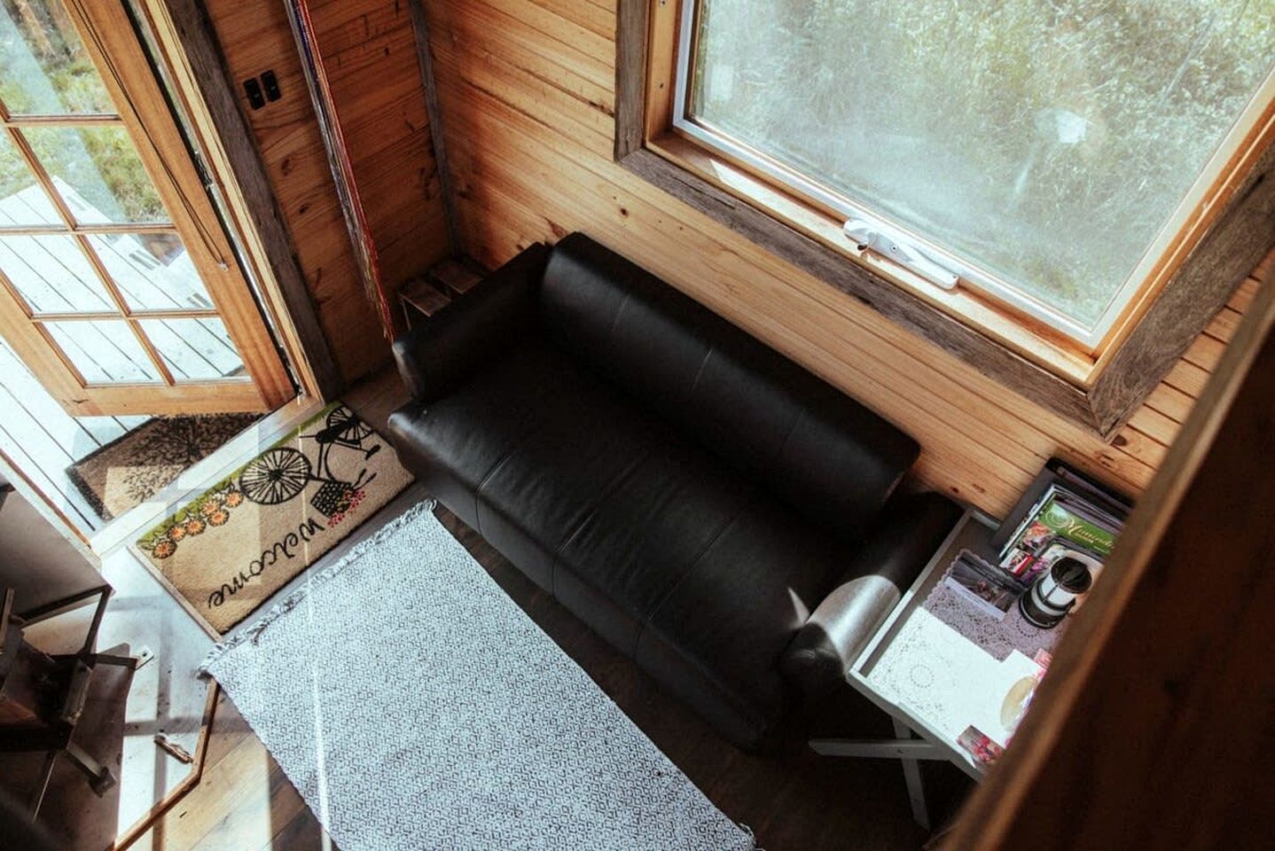 A compact room with a black sofa, a small table, and a window with a view of trees.