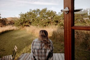 A person seated on a wooden deck with a view of a grassy field and trees.
