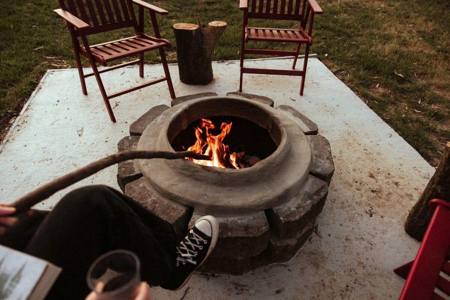 A fire pit with a metal bowl, surrounded by two wooden chairs and a wooden table.