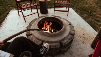 A fire pit with a metal bowl, surrounded by two wooden chairs and a wooden table.