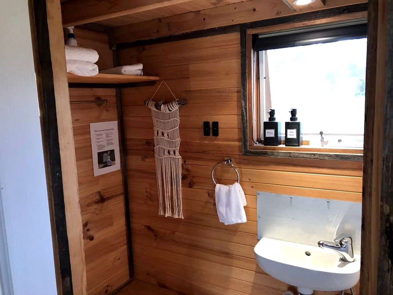 A wooden cabin bathroom with a sink, towel rack, and a window with bottles on the windowsill.