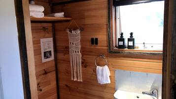 A wooden cabin bathroom with a sink, towel rack, and a window with bottles on the windowsill.