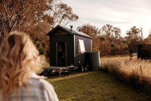 A small, single-story cabin with a metal roof, a sliding door, and a small porch area. - Yarra Valley Tiny House for Eco-Friendly Glamping in Victoria (Yea)