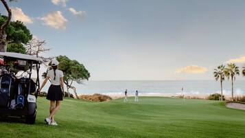Ein Golfplatz mit Blick auf den Ozean, ein Golfwagen und Spieler.