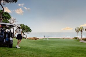 Ein Golfplatz mit Blick auf den Ozean, ein Golfwagen und Spieler.