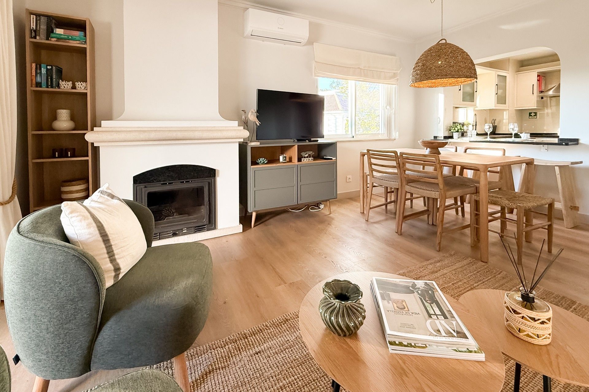 Ein Wohnzimmer mit Kamin, Fernseher, Essbereich mit Holzmöbeln und einer Küche im Hintergrund.