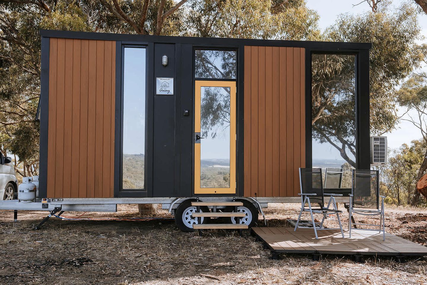 Een moderne, compacte stacaravan met een grote schuifdeur, een klein terrasje met stoelen, en een mooi uitzicht.