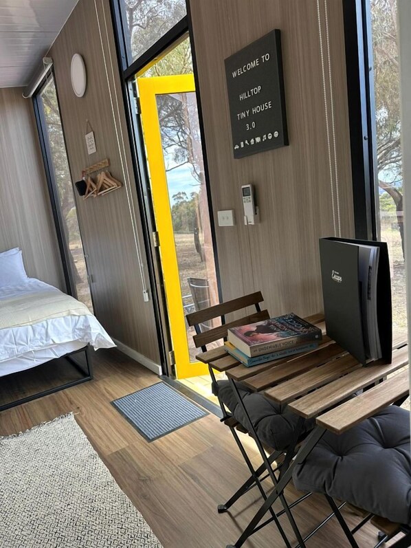 Una habitación moderna y compacta con una cama, un banco, una mesa y un televisor pequeño.