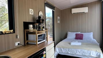 A hotel room with a bed, a small kitchenette, a microwave, a fan, and an air conditioning unit.