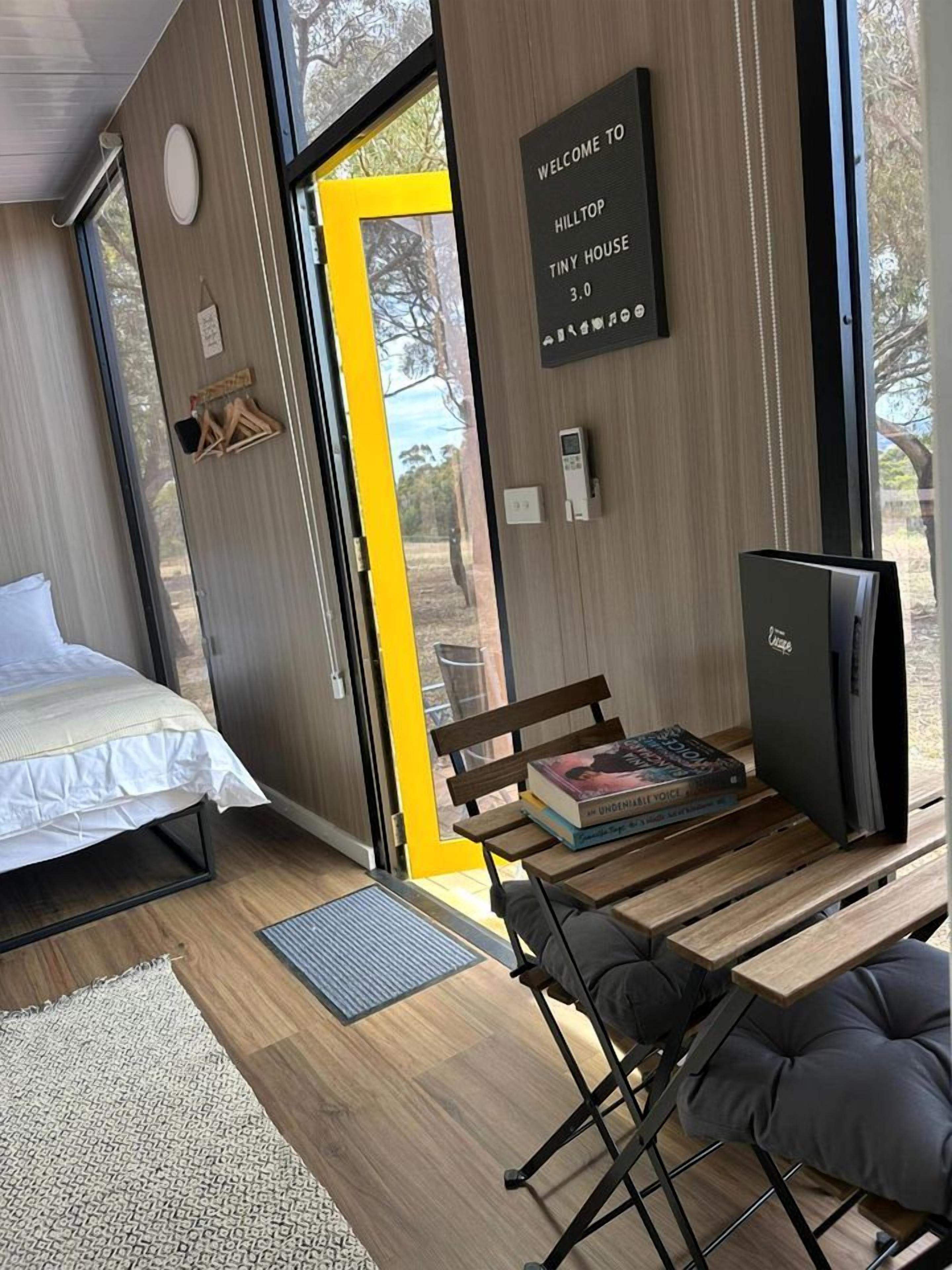 Una habitación moderna y compacta con una cama, un banco, una mesa y un televisor pequeño.