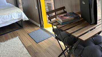 Una habitación moderna y compacta con una cama, un banco, una mesa y un televisor pequeño.