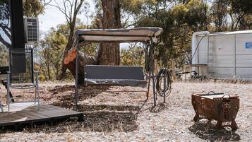 A rustic outdoor seating area with a metal bench and a covered table, surrounded by trees and dry grass.