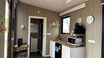 Una cocina compacta con microondas, lavamanos y un refrigerador pequeño. Hay una mesa de madera con sillas y una encimera blanca.