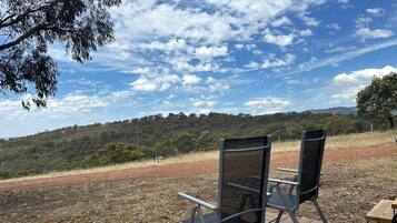 An outdoor seating area with two chairs and a table, overlooking a hilly landscape.