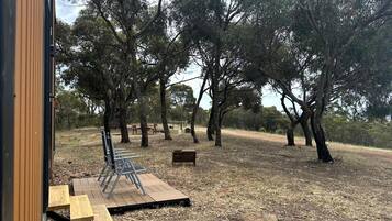 An outdoor seating area with wooden benches and metal chairs, surrounded by trees.