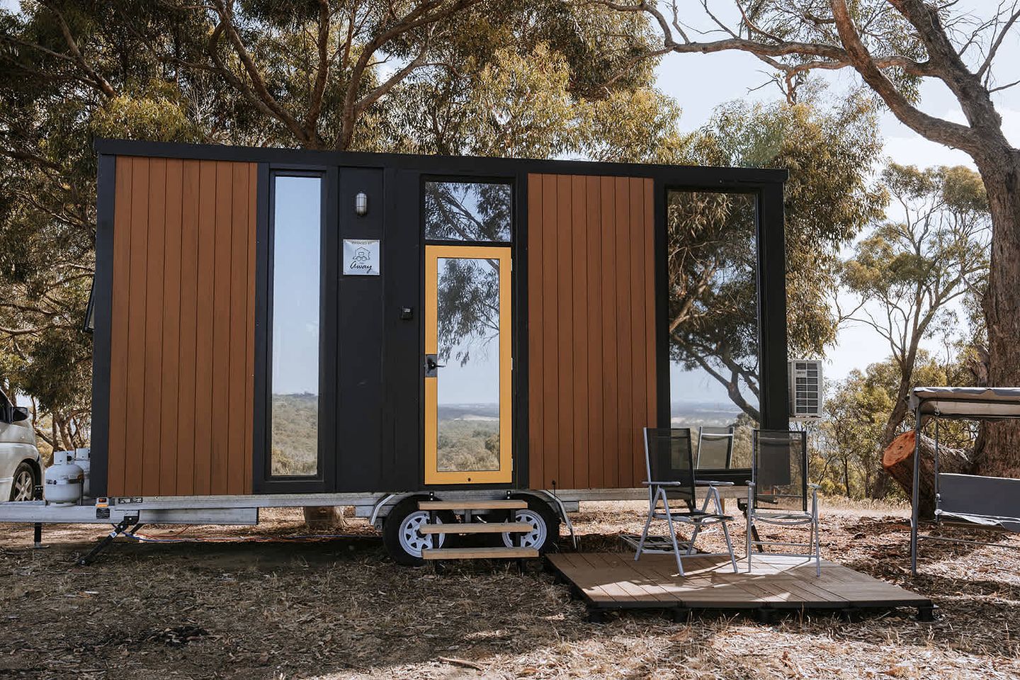 Eine kleine, moderne Holzhütte mit einer Schiebetür, einer kleinen Terrasse und Blick auf die umliegende Landschaft.