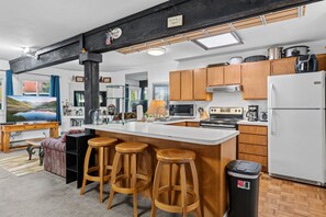 A modern kitchen with a central island, wooden stools, a refrigerator, and various appliances. - Gore Range Views and Trails Near Keystone Breck and Copper (Silverthorne)