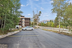 A parking lot with a building in the background, trees lining the area, and mountains in the distance. - Gore Range Views and Trails Near Keystone Breck and Copper (Silverthorne)