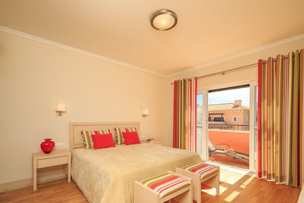 A hotel room with a bed, bedside tables, a lamp, a red vase, a bench, and a view of the outside.