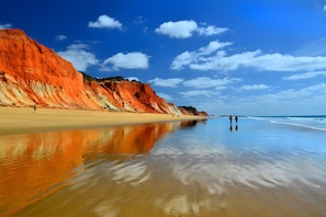 A beach with a long stretch of sand and a cliff with red and white layers.