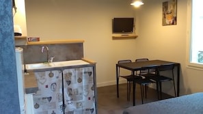 Una habitación compacta con kitchenette, una zona de comedor con mesa y sillas, un televisor montado en la pared y una ventana.