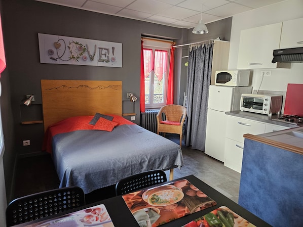 Habitación de hotel con cama, una mesa de comedor con sillas, kitchenette y vista al exterior.