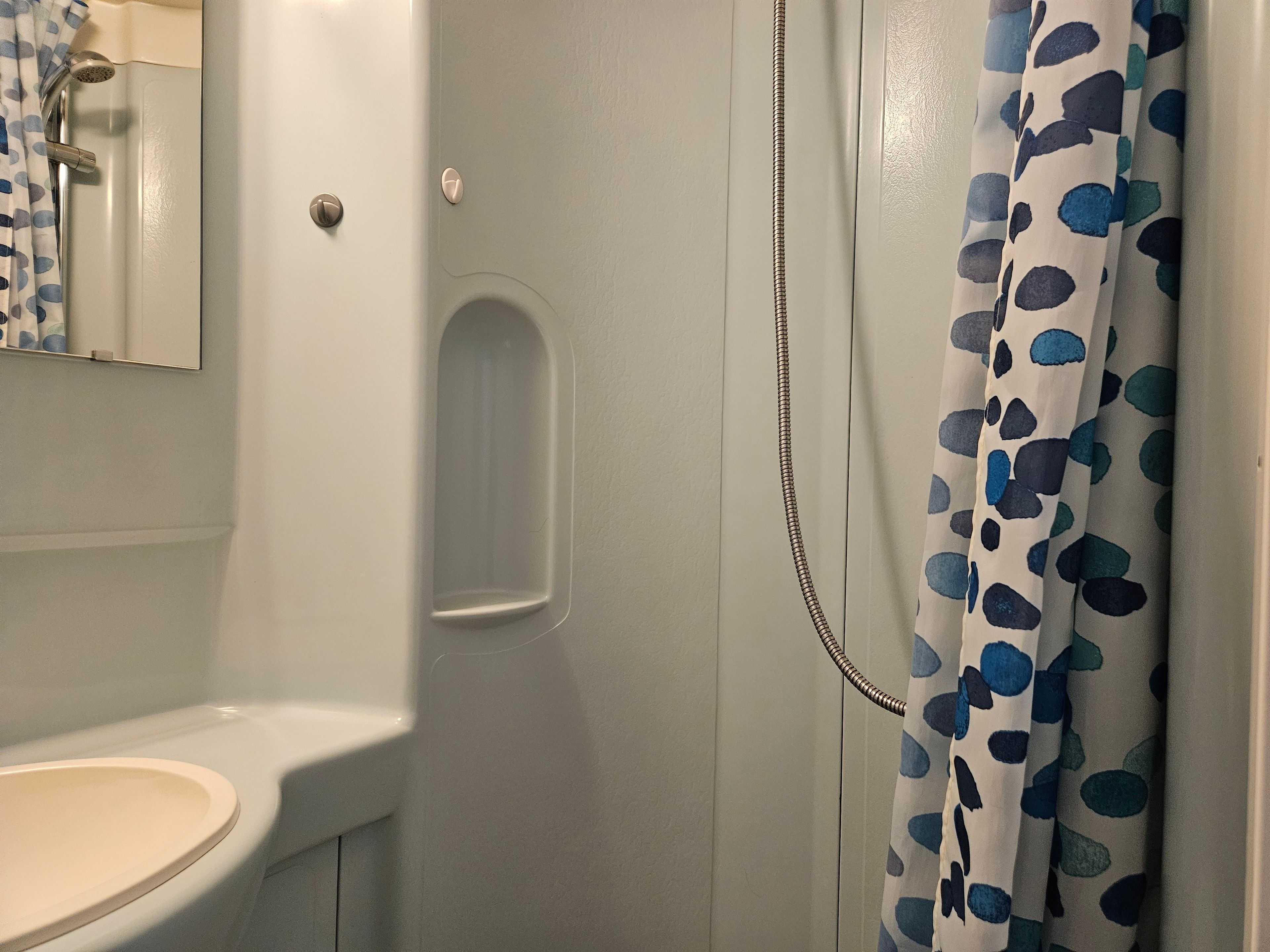 A bathroom with a white sink, a shower with a blue polka dot shower curtain, and a mirror above the sink.