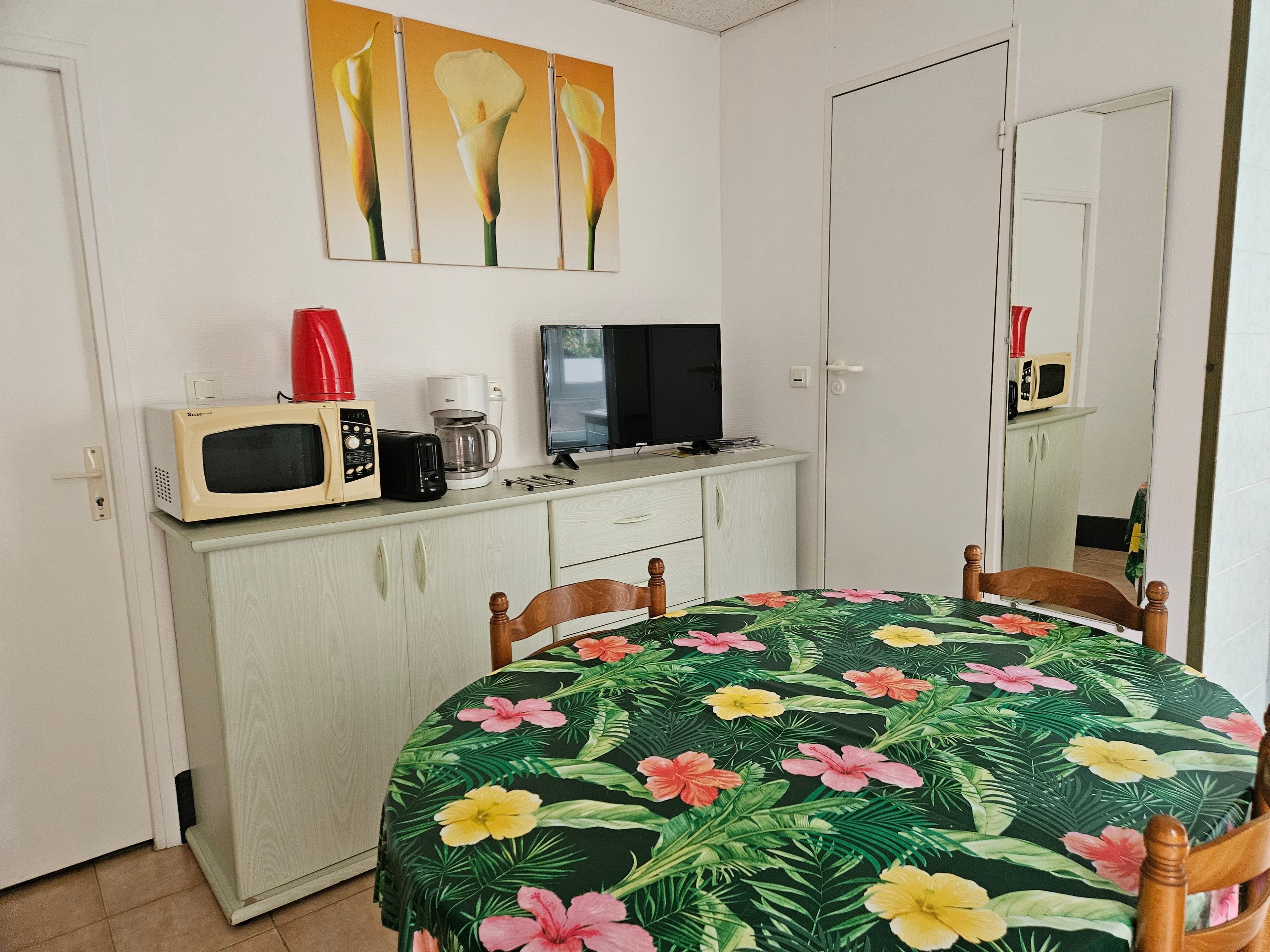 Une pièce comprenant une table à manger, des chaises, un four à micro-ondes, un grille-pain, une machine à café et un téléviseur posé sur un meuble.