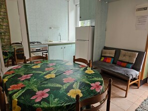 Et lille køkken med spiseplads, en sofa med hynder og et bord med blomstret dug.