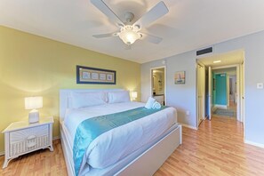 Quarto com cama, mesas de cabeceira, ventilador de teto e uma obra de arte na parede.