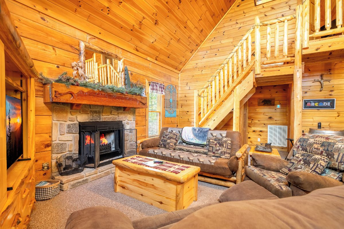 A log cabin interior with a stone fireplace, a sofa, a coffee table, and a staircase.