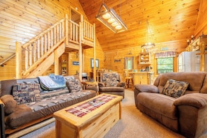A wooden cabin interior with a staircase, two sofas, a coffee table, and a kitchen area. - 🐻 Happy Bear | Arcade, Electric Fireplaces & Seasonal Community Pool (Sevierville)