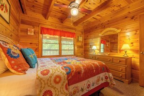 Ein Schlafzimmer einer Holzhütte mit Bett, Schminktisch und Deckenventilator.