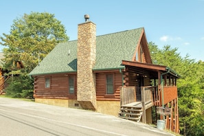 A log cabin with a stone chimney, a porch, and a staircase leading to the entrance. - 🌲 Cozy Cabin near Douglas Lake | Seasonal Pool | Sleeps 6 | Fireplace 🔥 (Sevierville)