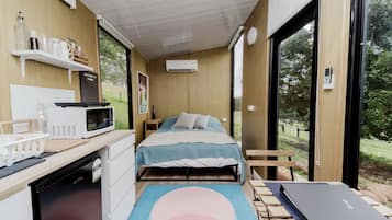 A compact bedroom with a bed, a desk with a microwave, and a large window.